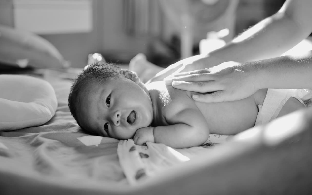 A parent's hand resting on a settled baby's chest and tummy