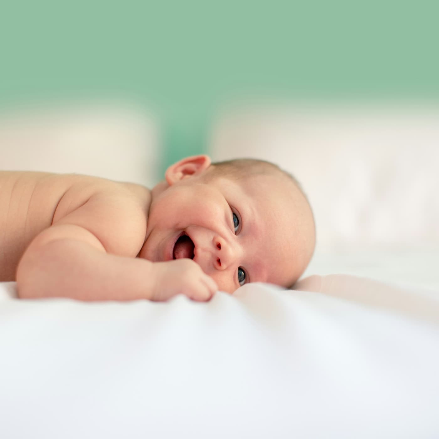 A baby lying on a bed, smiling up at the camera